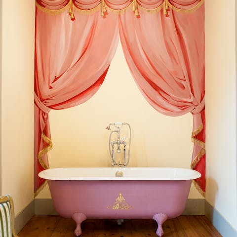 This blush pink roll top bath framed by a painted curtain mural