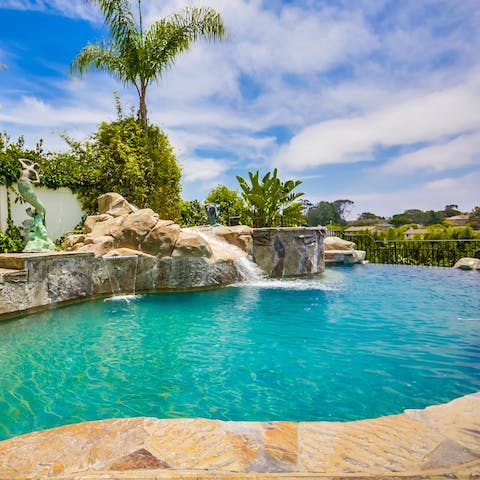 Swim in the pool with an elevated waterfall feature and slide 