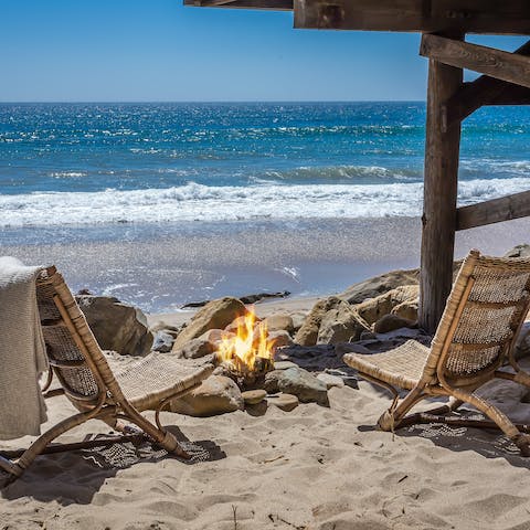 Cosy up round a beach bonfire as the sun sets over the ocean