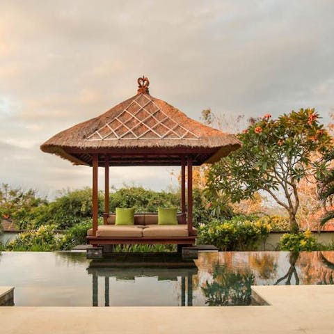 Relax in the dreamy thatched gazebo by the pool, surrounded by lush greenery 