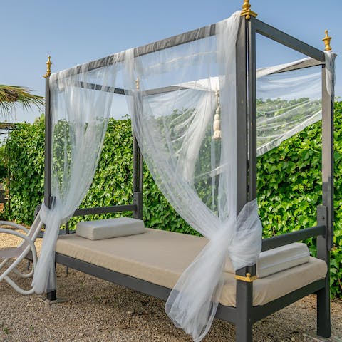 Lie back on the elegant, four-poster sun lounger with a cocktail