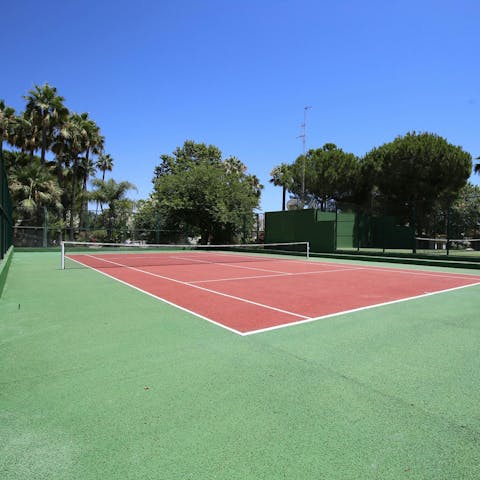 Have a match on the shared tennis court surrounded by palms and trees