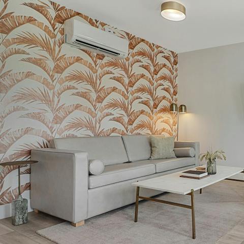 Escape the sun in the cool living room – we love the patterned wallpaper behind the sofa