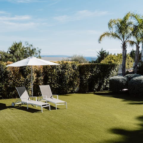 Rest under a sun umbrella on the immaculate lawn, with sea views in the distance